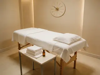 Massage bed with a wall clock, folded towels and a small oil bottle
